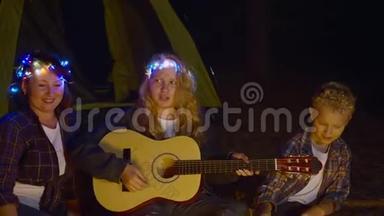 欢快的<strong>女孩弹吉他</strong>，一起唱着歌，妈妈和哥哥在夜林的篝火前。<strong>女孩</strong>